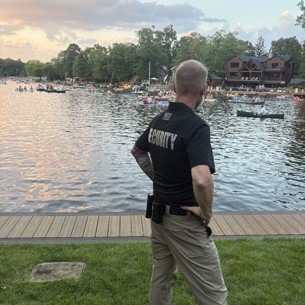 Security officer on post at a lakefront community event at dusk, watching the water